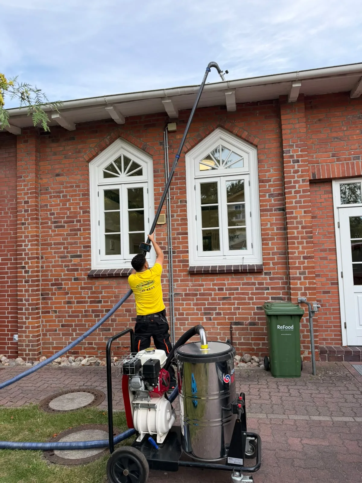 Blitz-Mitarbeiter reinigt eine Dachrinne am Backsteingebäude mit einem Saugsystem vom Boden aus