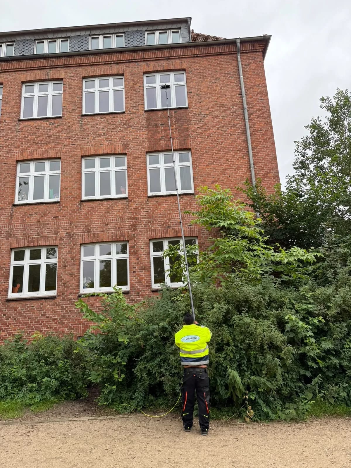 Fensterreinigung mit Teleskopstange an einem hohen Klinkergebäude