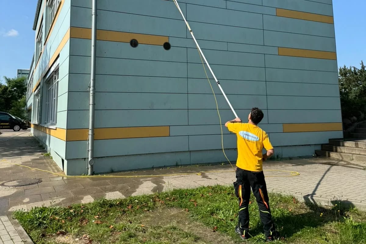 Blitz-Mitarbeiter mit Teleskopbürste an einer modernen Fassade